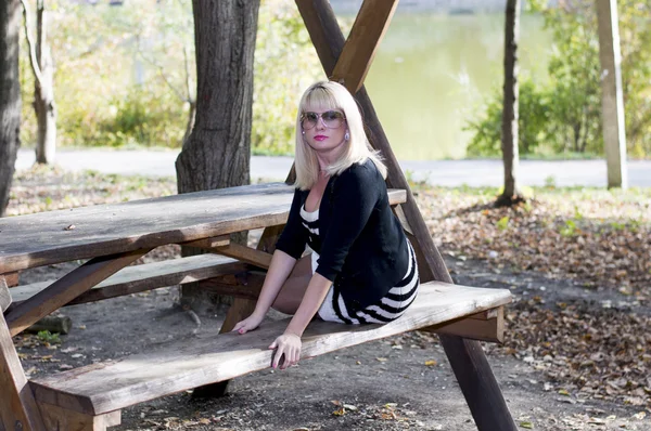 The beautiful blonde on a bench in park at the lake — Stock Photo, Image