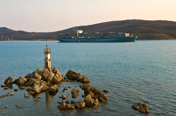 El buque portacontenedores Svend Maersk pasa por un pequeño faro al atardecer. Bahía Nakhodka. Mar del Este (Japón). 19.04.2014 — Foto de Stock