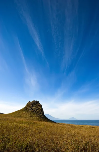 Yalnız dağ deniz kenarı mavi gökyüzü altında. — Stok fotoğraf