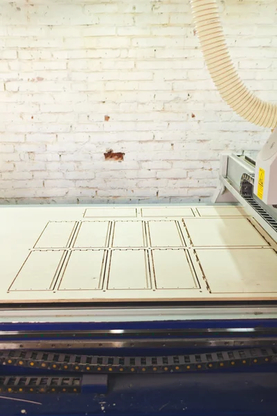 Pared de ladrillo blanco en taller y mesa CNC con producto de cubierta de madera con patrón en él y cinturones de la máquina debajo de él — Foto de Stock