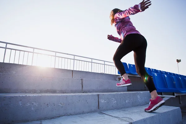 Young sporty woman in sportswear running upstairs with sunbeam on photo and sunset on background. Motivational photograph Stok Resim