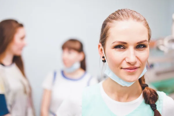 Young attractive woman dentist with mask on her neck smile friendly and cheerful with assistant and patient smiling on background talking after successful treatment procedure close-up portrait Telifsiz Stok Fotoğraflar