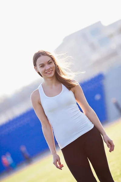 Fille sportive en vêtements de sport se tient souriant sur un stade après trainig vue d'angle — Photo