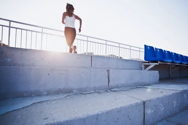 Молодая спортсменка в спортивной одежде бежит наверх на стадионе на закате. Обучение в городе — стоковое фото