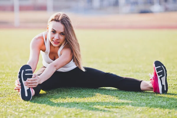 Ragazza sportiva che allunga le gambe sul campo — Foto Stock