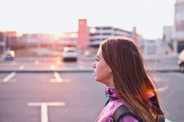 Attractive girl backpacker looking at sunset at parking lot on background side view with sunbeam Stok Resim