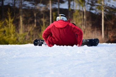 Kar kayakçısı dağın yamacında otururken dinleniyor. 
