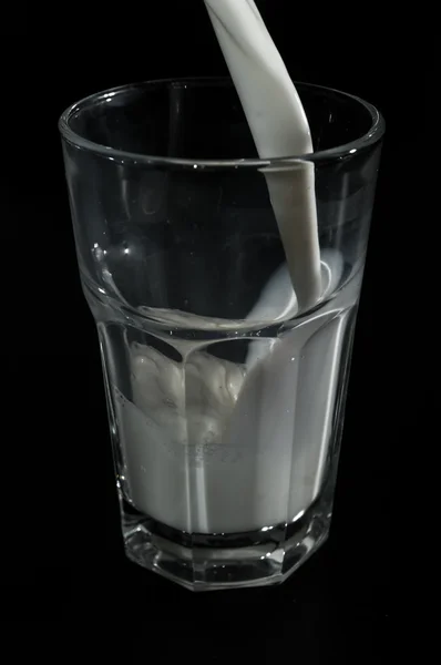 Milk poured into glass isolated on black background — Stock Photo, Image
