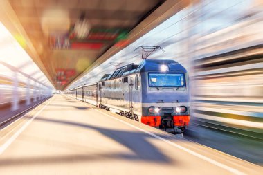 Yolcu treni olan öncü elektrikli lokomotif istasyondaki şehir platformundan yüksek hızda geçer.