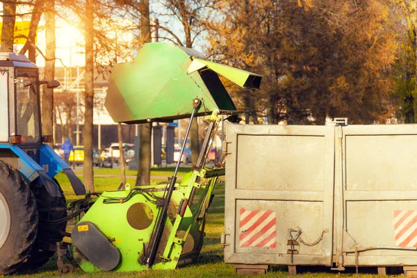 トラクターが牽引する真空スイーパーが秋の公園の街の仕事から葉を収穫するための容器にダンプ — ストック写真