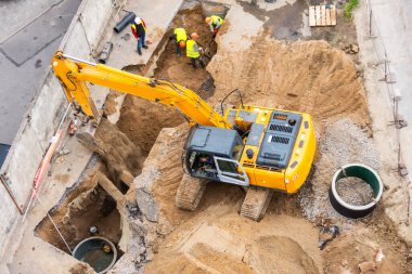 Bir inşaat sahasında kazıcı yükseltilmiş kovayla kanalizasyon ve drenaj boruları için hendek kazarken, üst hava manzarası