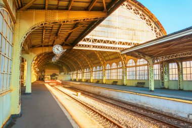 Büyük metal kemerli eski tren istasyonu manzarası ve güneşli bir günde insanlar için saati olan boş bir platform.