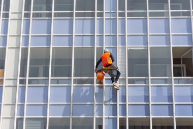 Binanın dışında, çok katlı bir binanın ön cephesini silip, camları silip süpürüyor.