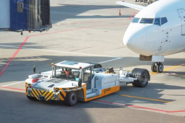 Uçak bakımı için özel ekipman kullanarak bir yolcu uçağını çekmek. Terminal binasının arka planında kalkış uçuşu