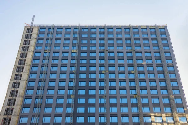 Facade cladding of a multi-storey building, many windows, and a construction elevator