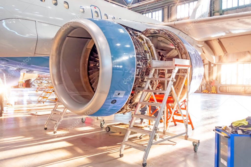 Opened aircraft engine in the hangar, illuminated by bright sunlight from outside the gate