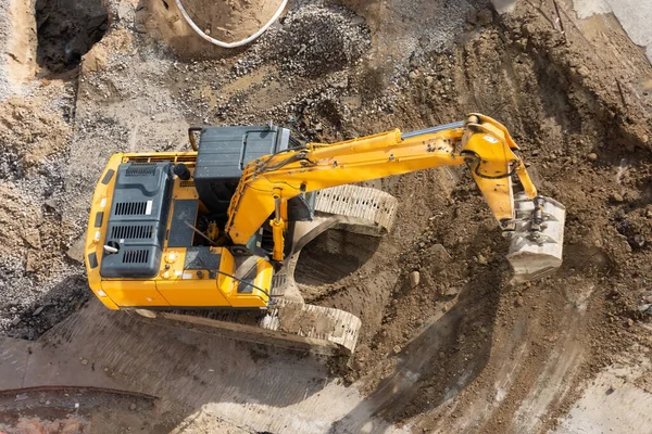 Excavator on the ground of a construction site with a raised bucket, top aerial view