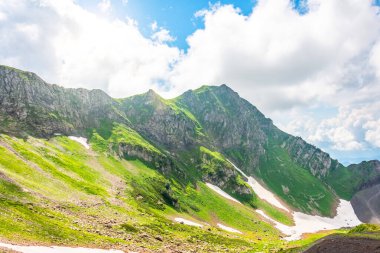 Yaz dağlarında çimen ve buz karları, tepelerin ve bulutların manzarası.