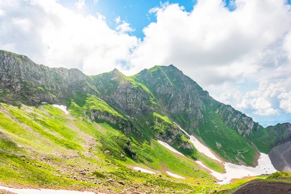 Yaz dağlarında çimen ve buz karları, tepelerin ve bulutların manzarası.