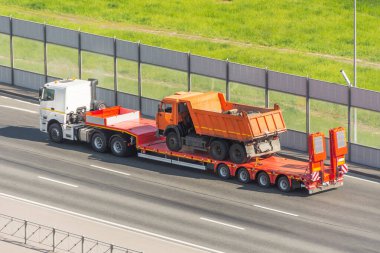 Vücudunda bir sürü toprak olan turuncu bir kamyon başka bir kamyonun yükleme platformuna nakledildi.