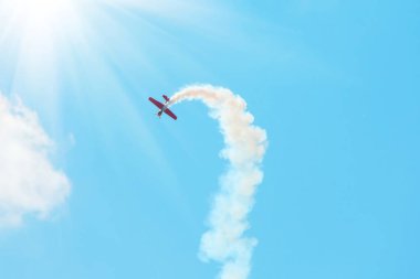 stunt plane trailing smoke bright sun and clouds