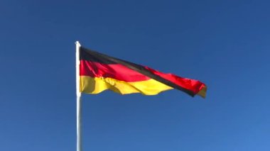 Mavi arka planda rüzgarda dalgalanan bayrak direğinde sallanan Almanya bayrağı