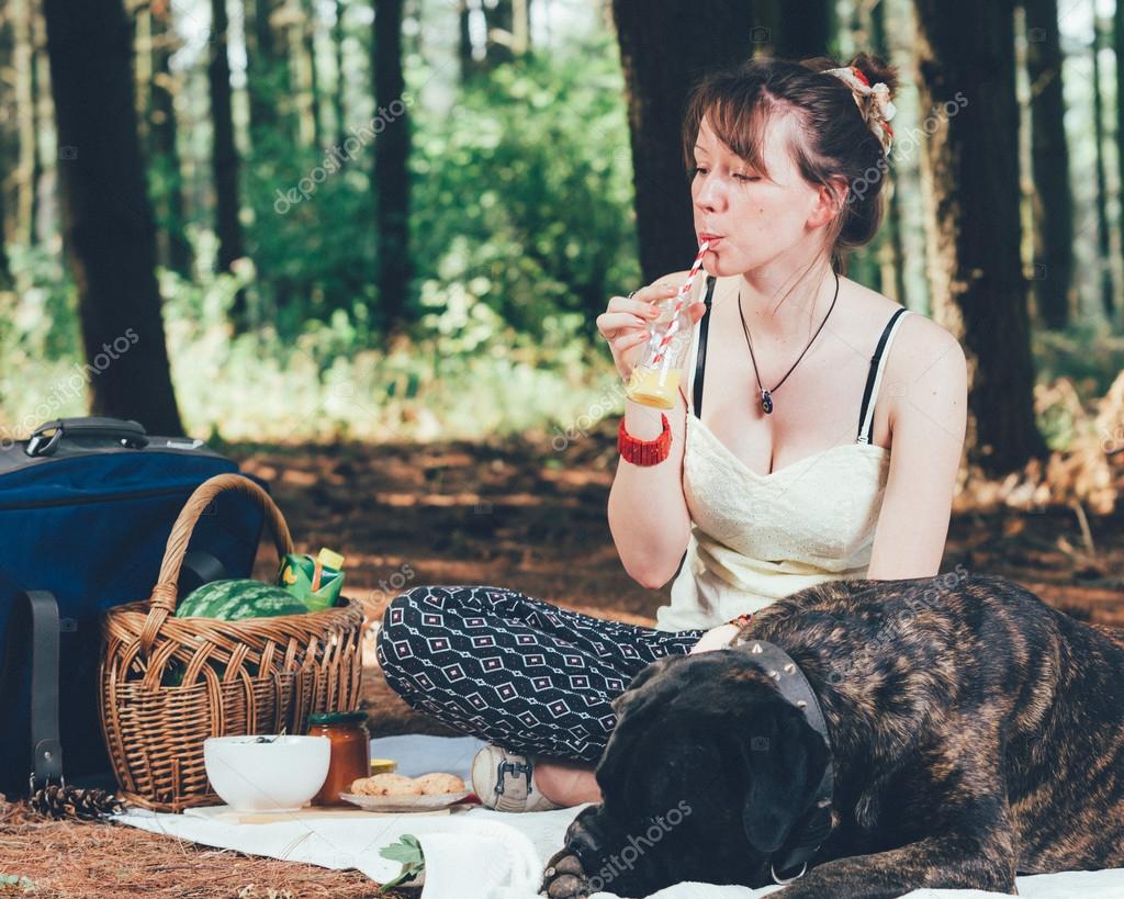 Girl on picnic with her dog drinking juice. — Stock Photo