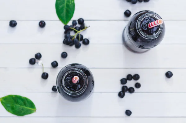 Cold delicious juice made of chokeberries on white wooden boards — Stock Photo, Image