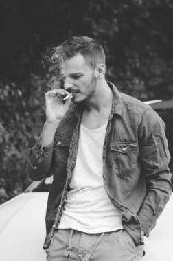 Beyaz bir t-shirt duman sigara forest yakınındaki yolda bir bıyıklı genç mülteci. Vintage retro tarzı etkisi, yumuşak odak, sığ Dof, düşük ışık, tahıl doku üzerinde en büyük boyutu görünür