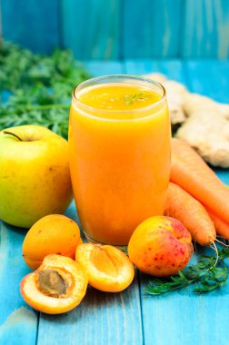 Glass of apricot, apple, carrot and ginger juice on colourful tu