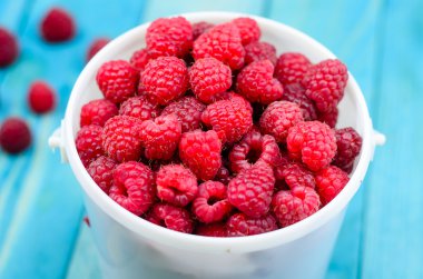Raspberry bucket on colourful turquoise blue painted wooden boar