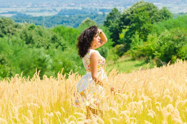 Buğday alanında çiçek elbise ile güzel bir kadın. Şehir manzarası — Stok fotoğraf