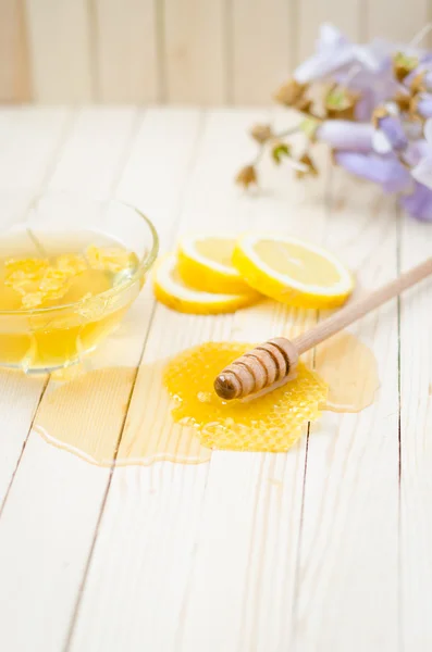 Honey dipper in honey with honeycomb, lemon, flowers — Stock fotografie