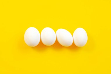 Ortadaki sarı arkaplanda beyaz yumurtalar, üst manzara, kopyalama alanı. Sarı arka planda çiğ yumurta, kopyalama alanı, üst manzara. Sarı arka planda beyaz yumurta, üst manzara. Tasarım, minimalizm, güzel sanatlar.