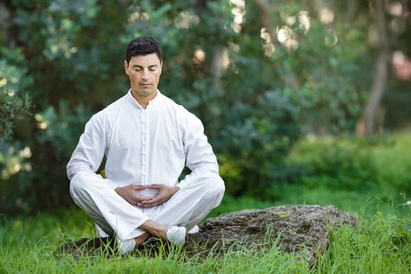 Man gör meditation sittande på stenen utomhus Royaltyfria Stockfoton