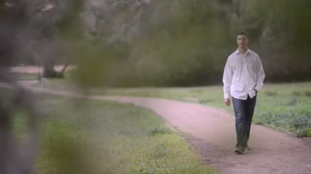 Молодой человек разговаривает по телефону в парке — стоковое видео
