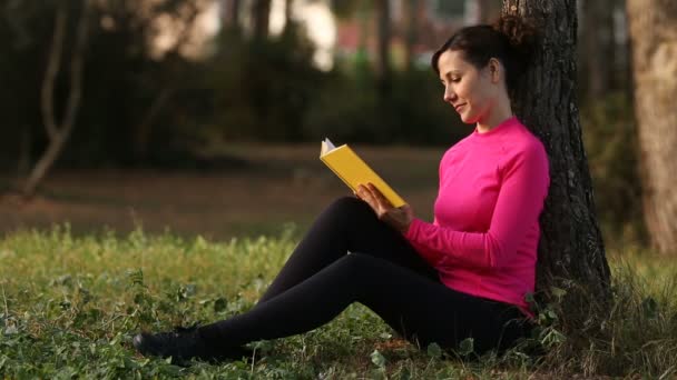 Junge Frau liest Buch im grünen Park — Stockvideo