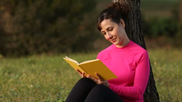 Молодая белая женщина читает книгу в зеленом парке — стоковое видео