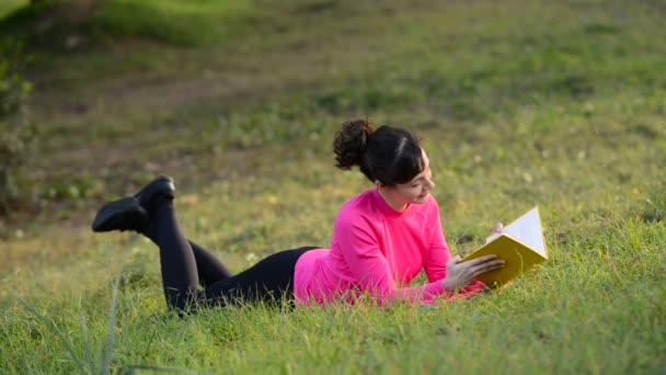 若い女性が草原に寝転がって本を読んで — ストック動画