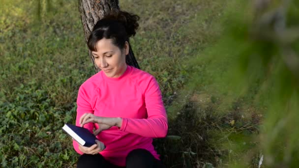 Mujer caucásica leyendo libro en el parque — Vídeos de Stock