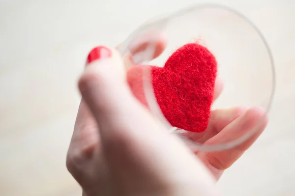 Kvinnans hand håller glaset med filt rött hjärta — Stockfoto