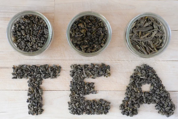 Assortment of dry green tea leaves in jars with letters made of tea leaves — Stock Photo, Image