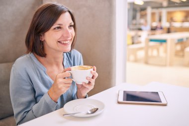 beautiful mature woman smiling while holding her coffee at table clipart