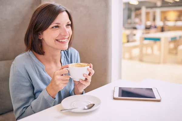 Beautiful mature woman smiling while holding her coffee at table — Stock Photo, Image