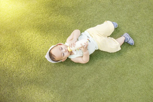 Asian baby drinking milk from bottle while he's laying on the gr — Stock Photo, Image