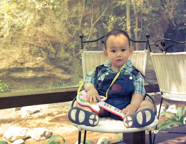 Baby sitting on a chair beside the creek in his hand holding gui — Φωτογραφία Αρχείου