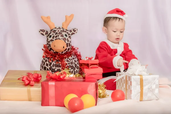 Kid no terno de Papai Noel sentado com boneca de rena entre th — Fotografia de Stock