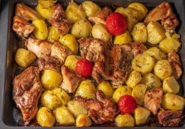 Fırın manzarasında fırında pişirilmiş taze patates, tavuk, hindi, domates parçaları.
