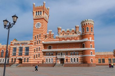 Büyük kırmızı tuğladan bir kale. Meydanda saat ve kaldırım taşları var.