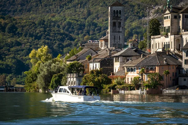 Orta (Novara), İtalya - 8 Ekim 2020: Orta San Giulio Adası 'nın bir kısmının panoraması, Orta Gölü, Kuzey İtalya' da küçük bir göl, Piedmont bölgesi, manastır rahibelerine ev sahipliği yapar. Bir turist teknesi göl sularında yüzüyor..